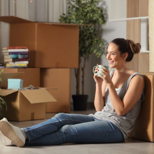 Una giovane donna rilassata siede sul pavimento con alcuni scatoloni da trasloco