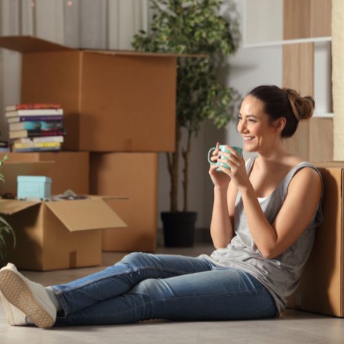 Eine entspannte junge Frau sitzt mit Umzugskartons auf dem Boden